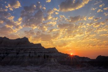 Early morning sun rays peek over Badlands formations.